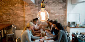 Group of business people brainstorming at a creative office and a light bulb in the foreground.