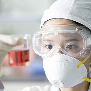 Female scientist in laboratory wearing protective glasses looking at a glass of solution.