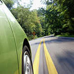 Close-up of green car speeding along a leafy road, captured with slight motion blur.