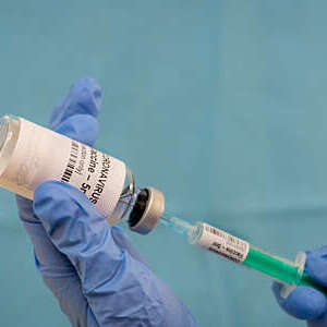 Doctor’s gloved hands draw a dose of coronavirus vaccine from a glass vial with a syringe.
