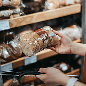 Young Asian woman carrying a shopping basket grocery shopping in a supermarket, shopping for packaged fresh wholegrain bread in the bread aisle. 