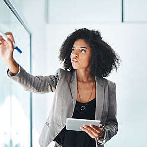 Shot of a young businesswoman using a digital tablet while writing notes on a glass wall in an office.