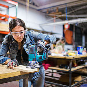 Female carpenter cutting wood using a power saw in a workshop. Los Angeles, October 2016